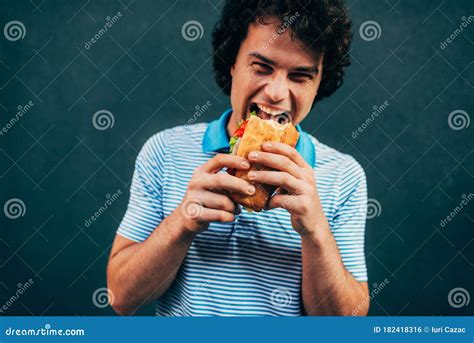 Happy Hungry Young Man Eating A Cheeseburger Has A Pleasant Expression