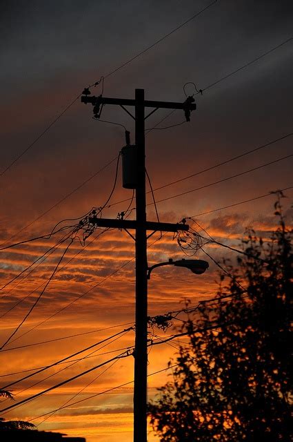 The Sun Is Setting Behind Power Lines And Telephone Poles With Trees