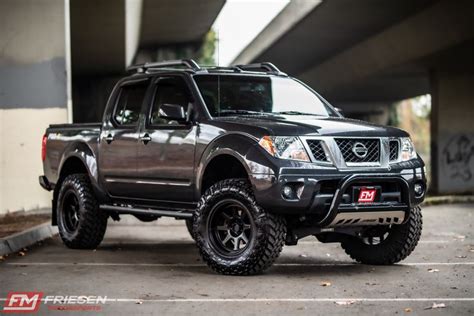 A Black Nissan Truck Parked In A Parking Lot Next To An Overpass And Bridge