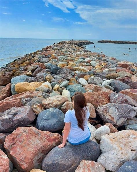 A Woman Sitting On Rocks Near The Ocean