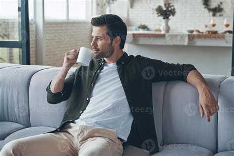 Thoughtful Young Man Drinking Coffee And Looking Away While Sitting On