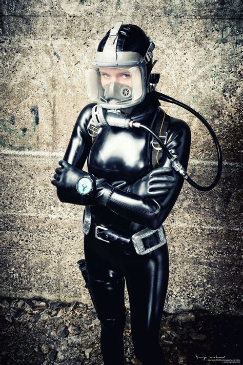 a person in a black suit and helmet with a hose attached to their head standing next to a wall