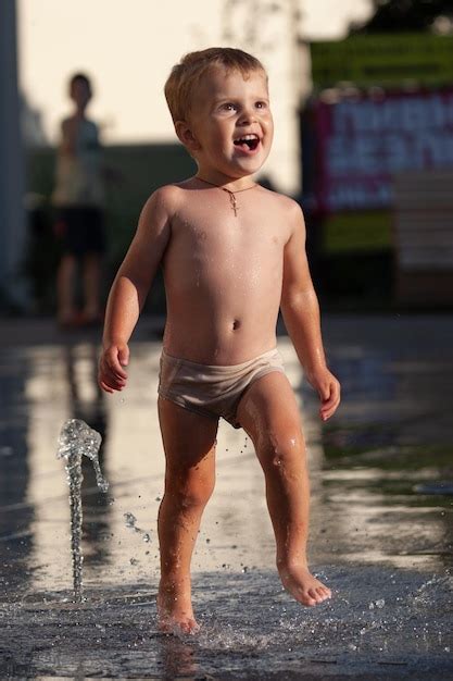 Un niño feliz juega con un chorro de agua en una fuente Foto Premium