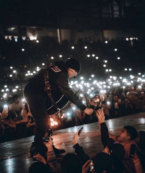 a man is performing on stage with his hands in the air while people are holding up their cell phones