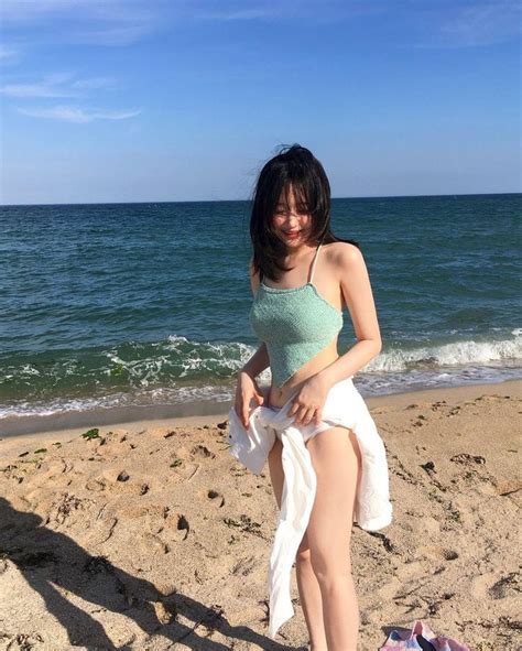 A Woman Sitting On Top Of A Sandy Beach Next To The Ocean Holding A Towel