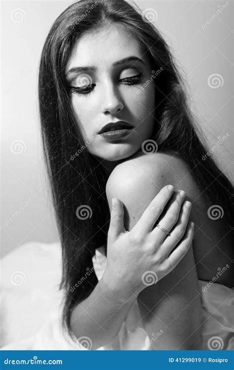 Portrait Of Seductive Woman Touching Her Naked Shoulder Looking Down Sitting On White Bed Black