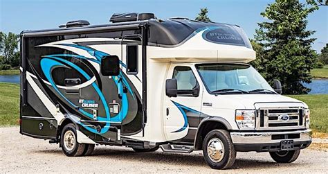 An Rv Parked On The Side Of A Road Next To A Body Of Water With Trees