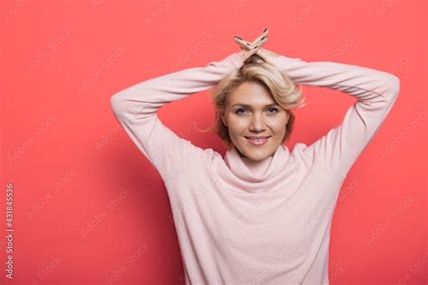 Charming Blonde Woman On A Red Studio Wall Is Smiling At Camera Holding Hands On Head Stock