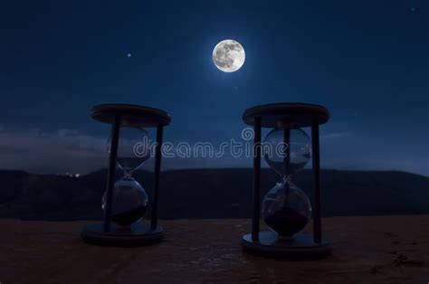 Time Concept With A Hourglass At Night With Moon Or Sand Passing Through The Glass Bulbs Of An