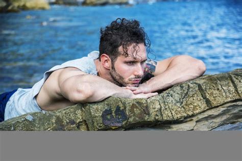 Homem Muscular Considerável Na Praia Que Senta se Em Rochas Foto de