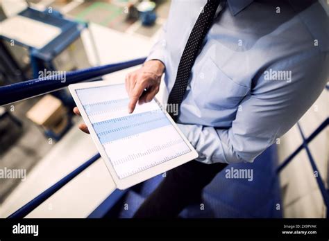 Manager Standing In Modern Industrial Factory Scrolling On Tablet