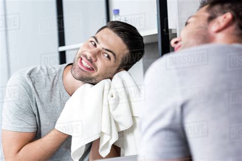 Happy Young Man Looking At Mirror And Wiping Face With Towel Stock