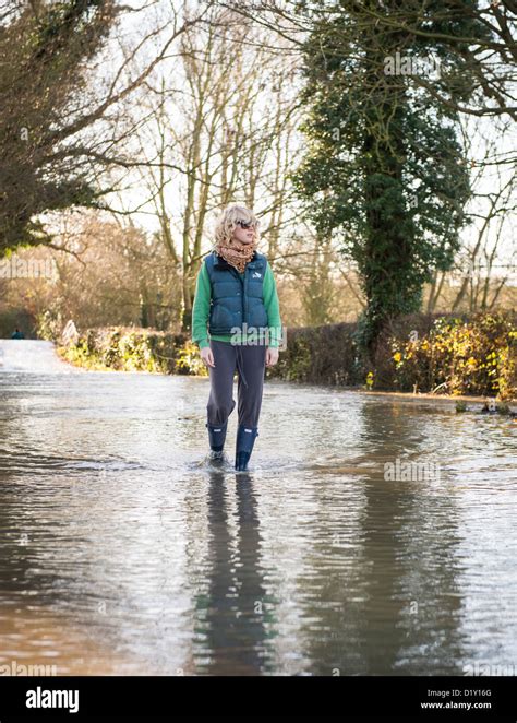 Frau In Gummistiefel Zu Fuß Durch Hochwasser Auf Einer Straße In Warwickshire Stockfotografie