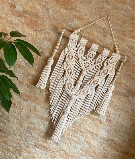 A Wall Hanging Made Out Of Macrame Beads And Tassels On A Brick Wall