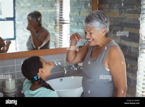 Grandmother And Granddaughter Brushing Teeth In The Bathroom At Home