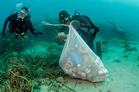 Scuba Divers Picking Up Cans And Garbage From A Coral Reef Offshore