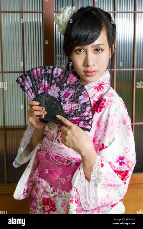 Asian Woman Wearing A Kimono In Front Of Japanese House Holding Fan