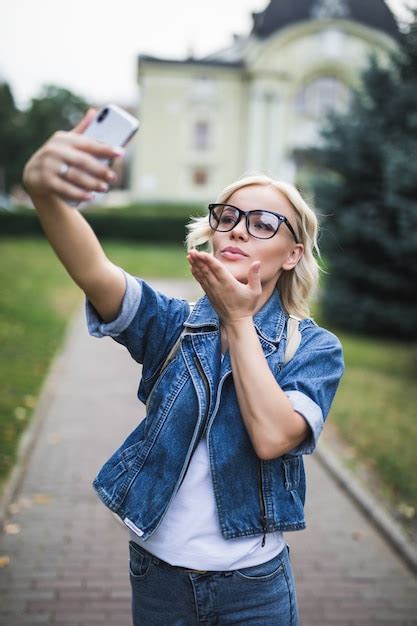 Mode élégante Fille Blonde Femme En Suite De Jeans Fait Selfie Donner Airkiss Sur Son Téléphone