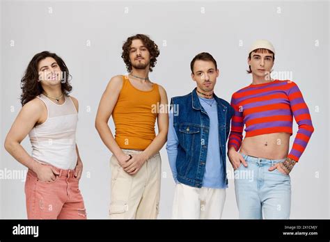 Four Joyful Good Looking Gay Men In Vivid Attires Smiling At Camera While Posing On Gray