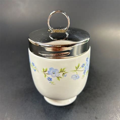 A White Container With Blue Flowers And A Silver Ring On The Lid Is Sitting On A Table