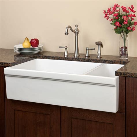 A White Sink Sitting Under A Faucet Next To A Bowl Of Fruit And Flowers