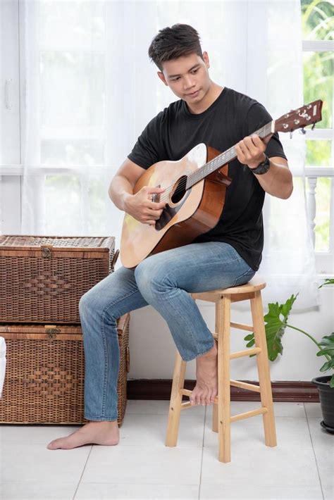 Un Hombre Sentado Y Tocando La Guitarra En Una Silla Foto De