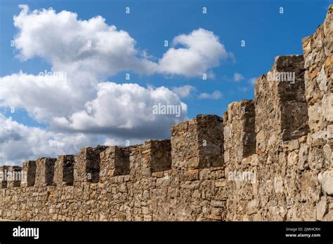 A Curved Castle Wall And Battlements Under A Blue Sky With White