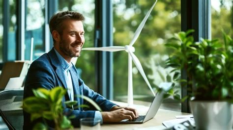 Smiling Man Working On A Laptop In An Office With Plants And A Wind