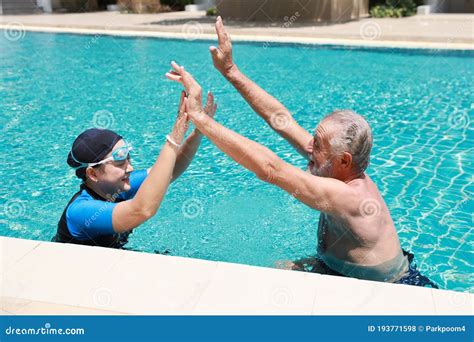 Happy Elderly Caucasian Husband And Elderly Asian Wife Take A Break While Swimming In Pool