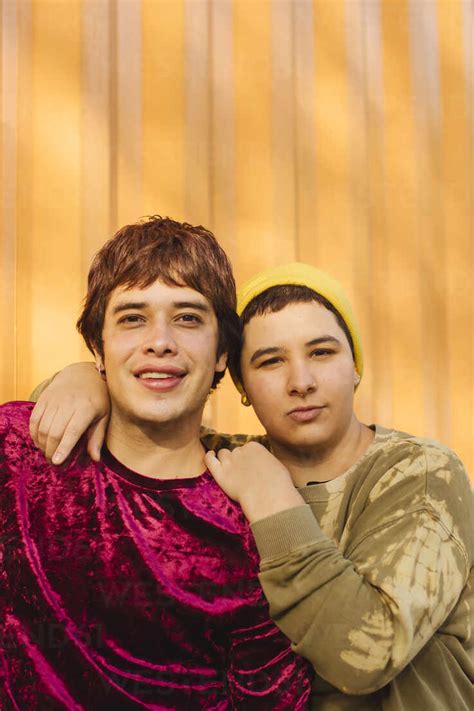 Happy Non Binary Couple Standing Together In Front Of Yellow Corrugated