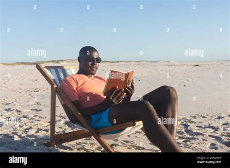 Happy African American Man In Sunglasses Sitting In Deckchair Reading