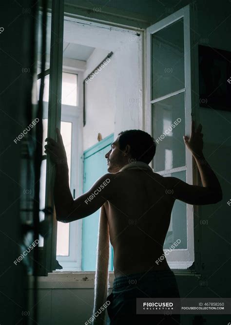 Back View Of Male With Naked Torso Standing Near Window At Home And Looking Away Quiet