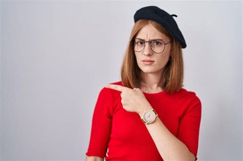 Premium Photo Young Redhead Woman Standing Wearing Glasses And Beret Pointing Aside Worried