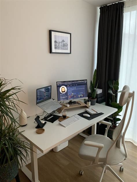 An Office Desk With Two Computers On It And A Potted Plant In The Corner