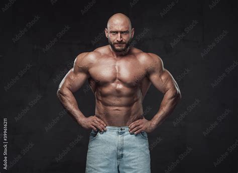 Powerful And Handsome Bodybuilder With Hairless Head Poses In Dark Background With Naked Torso