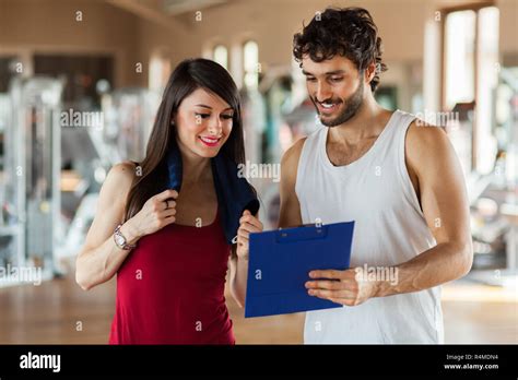 Young Woman Talking To Her Fitness Trainer In The Gym As They Consult A