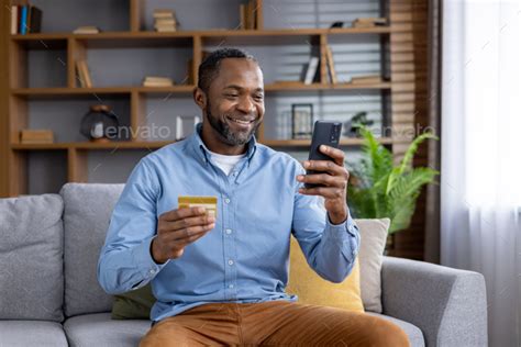 Joyful Mature Man At Home On Sofa With Phone And Bank Credit Debit Card