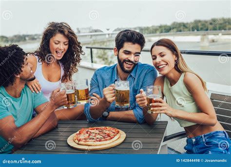 Group Of Young Cheerful People Eating Pizza And Drinking Beer While