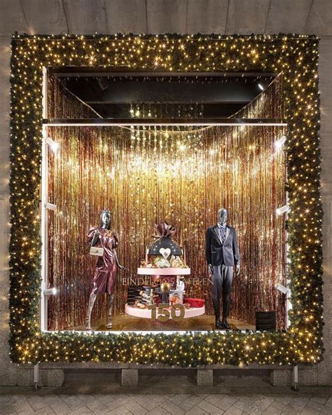 Two Mannequins In Front Of A Window With Gold Tinsel And Lights