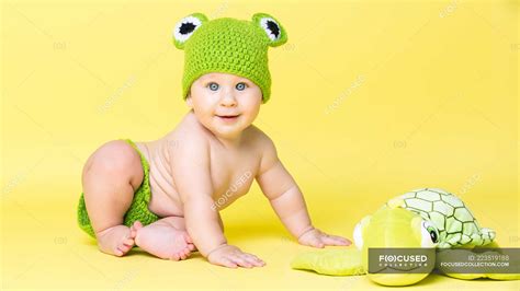 Adorable Little Boy In Frog Hat Sitting At Turtle Toy On Yellow