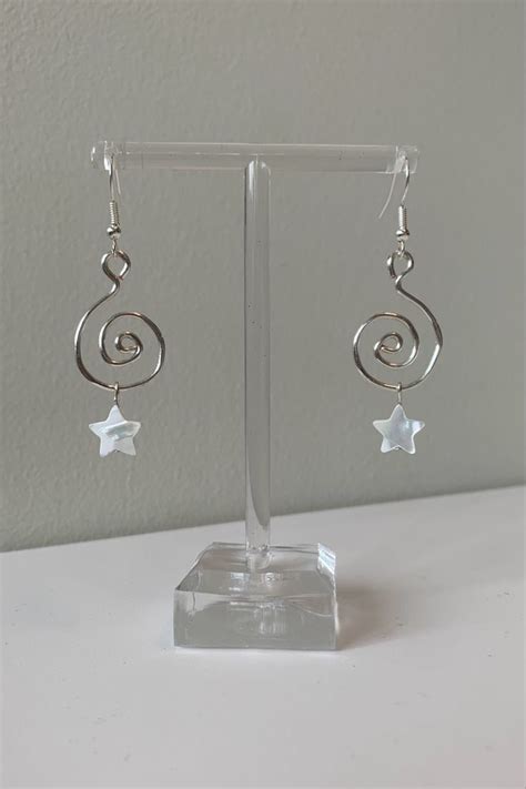 Silver Earrings With White Stars Hanging From Them On A Clear Display