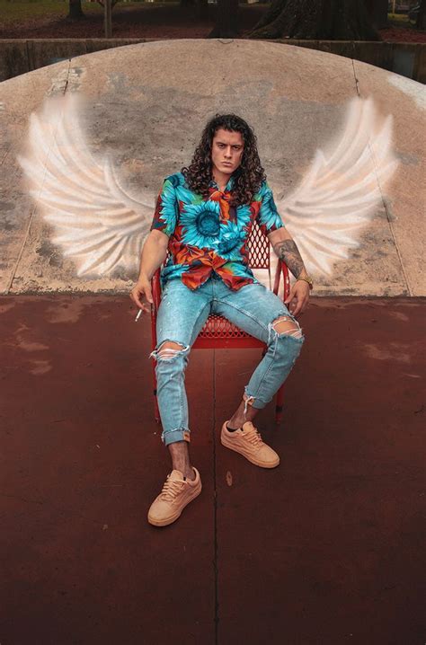 A Man Sitting On Top Of A Red Chair Next To An Angel Wings Mural In The