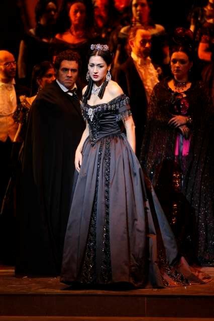 A Woman In A Black Dress Standing On Stage With Other People Behind Her