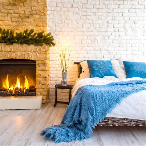 Bed With Blue Pillows And Coverlet Near Fireplace Against White Brick