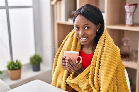 Young African American Woman Drinking Coffee Sitting On Table At Home