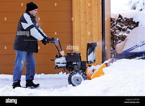 A Man Uses A Snowblower To Clear Snow In Front Of A Driveway Stock