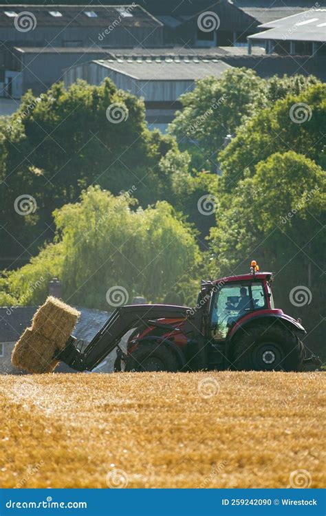 Tractor Collecting Bales Of Hay In A Field With Green Trees And