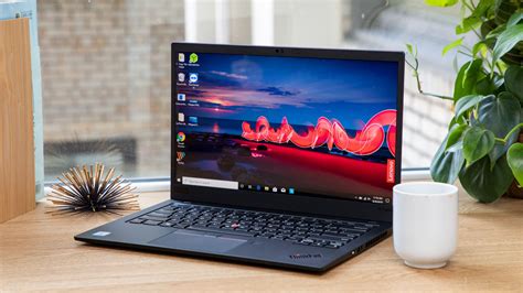 An Open Laptop Computer Sitting On Top Of A Wooden Desk Next To A Cup