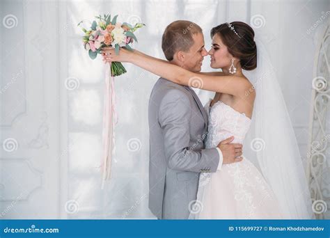 The Bride Hugs The Groom And Holds A Bouquet Of Flowers In Her Hands A