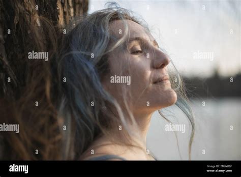 Close up gray hair woman with half closed eyes leaning against tree ...